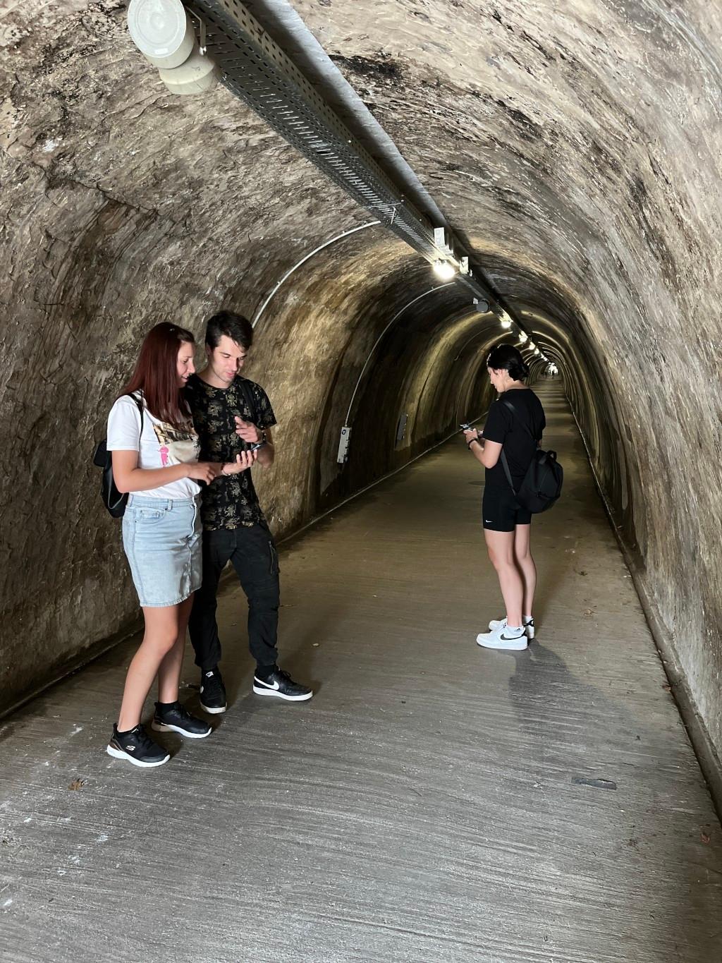 A man and a two women on their phone solving clues. They are in a tunnel.